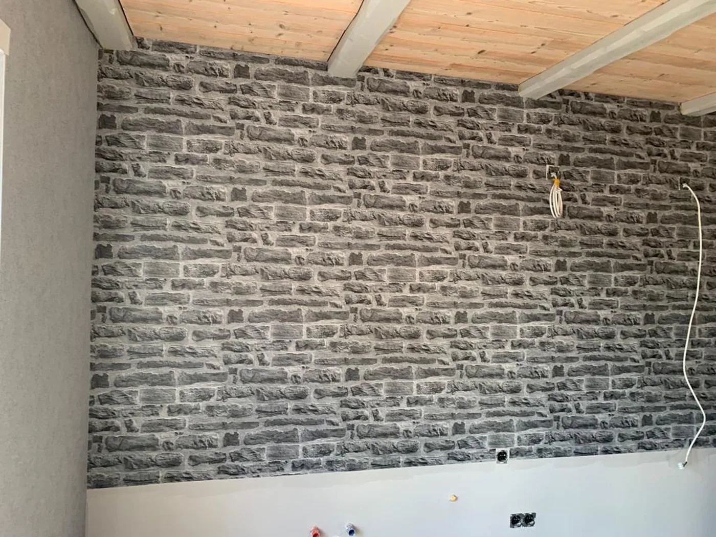 Wand mit Tapete in Natursteinoptik unter einer Holzdecke